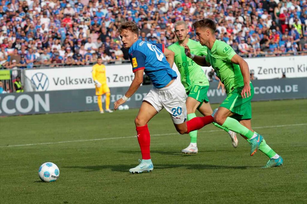 Fiete Arp (Holstein Kiel, hier von Kilian Fischer (re., VfL Wolfsburg) verfolgt, steht gleich woanders im Mittelpunkt. © 2024 Ismail Yesilyurt