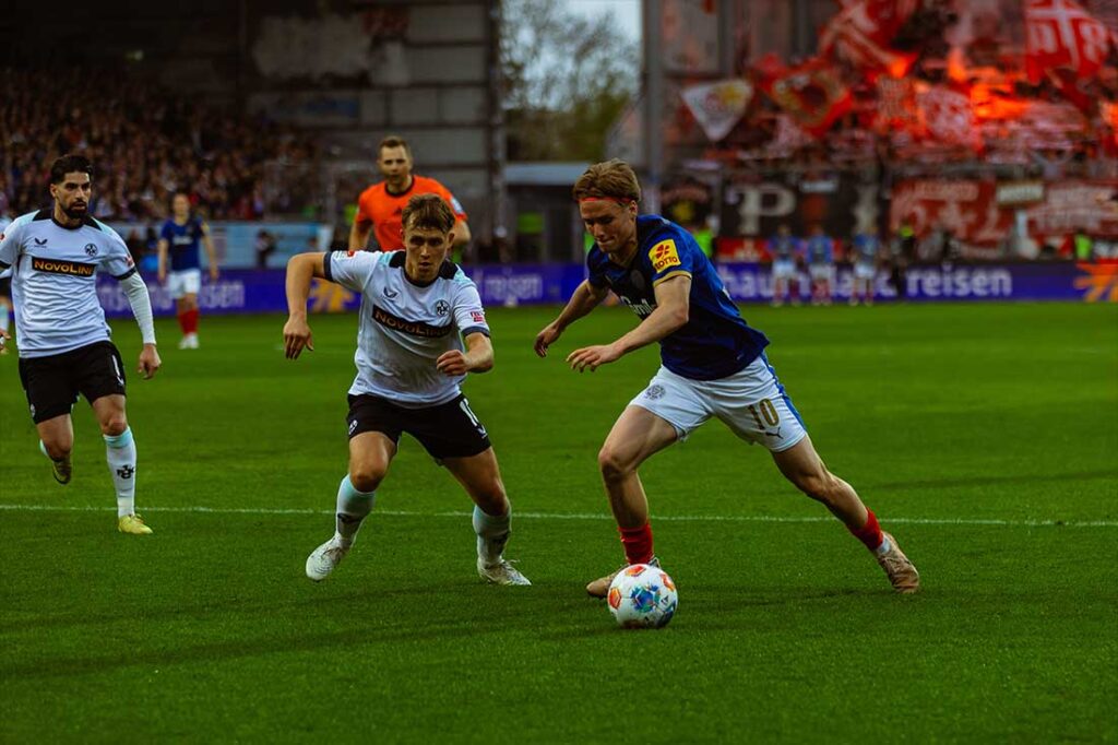 Der eingewechselte Jonas Therkelsen (Holstein Kiel) bringt ordentlich Schwung mit. Links Naatan Skyttä (1. FC kaiserslautern) im Zweikampf mit dem Kieler. 11ven Pixel