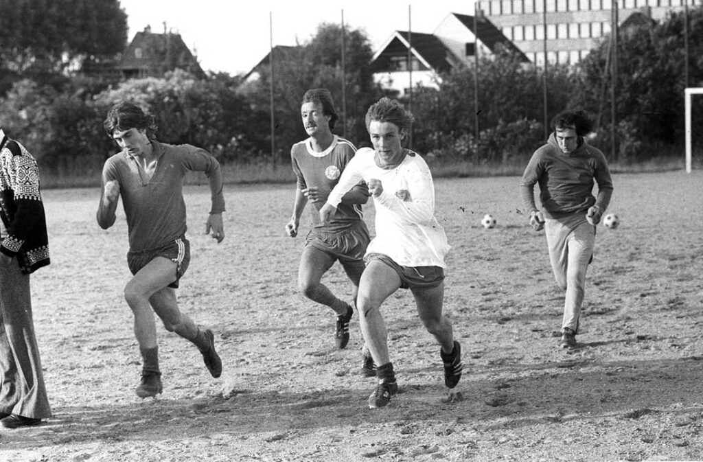 Saisonvorbereitung 1974 auf dem staubigen und trockenen Fögeplatz, Blickrichtung Projensdorfer Straße. Dietmar Tönsfeldt und Thorsten Neumann sprinten vor Dieter Reh und Egbert Landsberg. Der Hammerwurfkäfig, der sich ungefähr hinter Tönsfeldt befand, ist nicht mehr vorhanden.